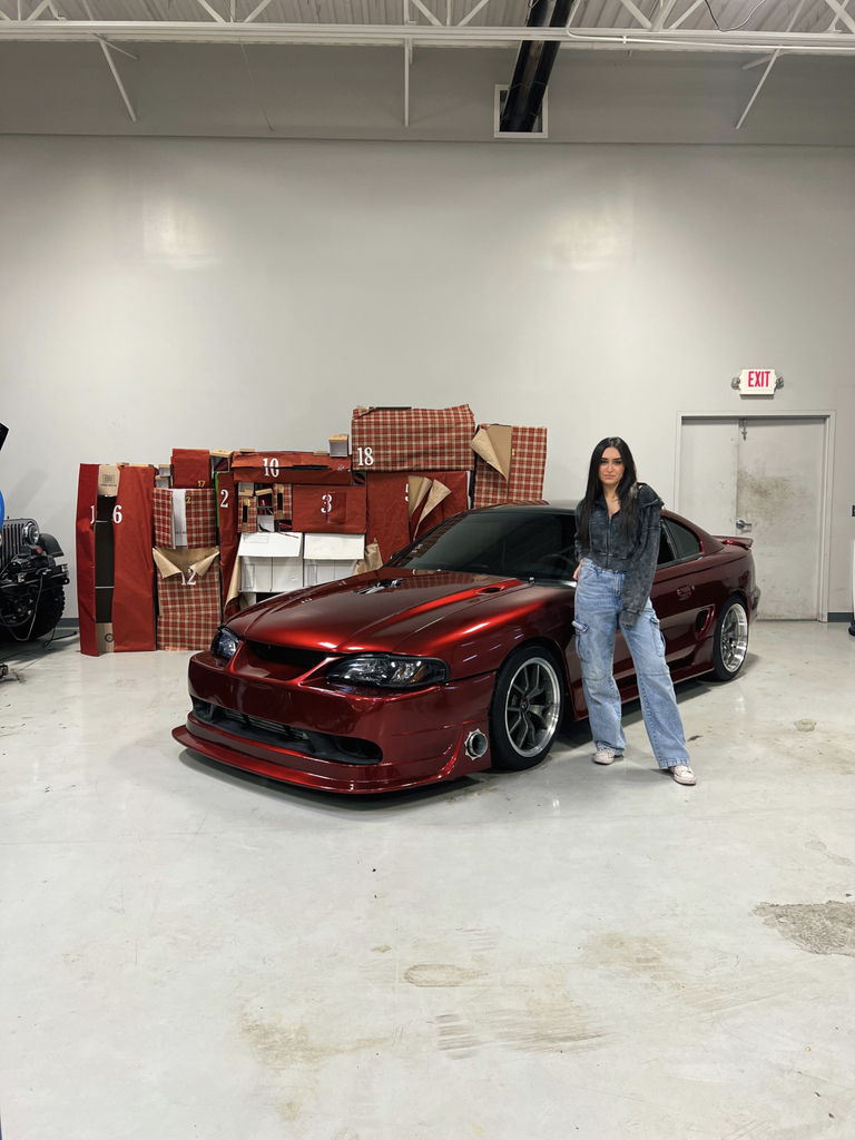 Christina Roki standing to the left of a red 1995 Ford Mustang.